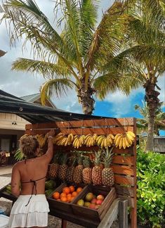 a woman standing in front of a fruit stand with bananas and oranges on it