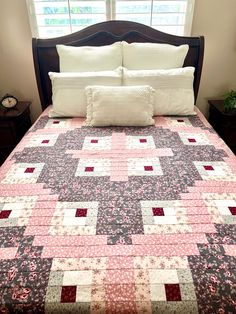 a bed with a pink and black quilt on it's headboard next to a window