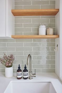 a kitchen sink with two bottles on the counter next to it and some shelves above