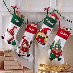 three christmas stockings hanging from a fireplace with personalized decorations on them and presents underneath