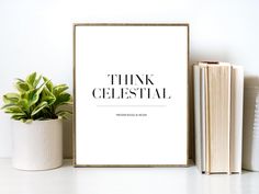 a white framed poster with the words think celestial next to some books and a potted plant