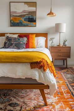 a bed with yellow blankets and pillows on top of it next to a painting hanging above the bed