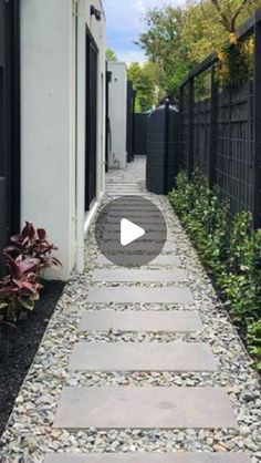 a stone path leading to a house with black fence and plants on either side of it