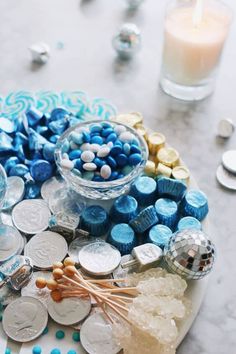 blue and white candies on a plate next to some silver coins, candles and candy