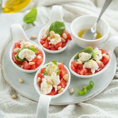 four small bowls filled with food on top of a white plate next to a spoon