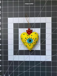 a yellow heart shaped ornament hanging on a piece of fabric next to a ruler