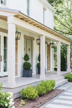 the front porch of a white house with potted plants