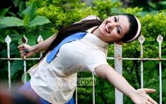 a woman with long hair and blue overalls posing for a photo in front of a fence