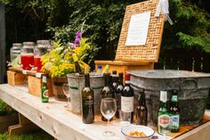 an outdoor picnic table with bottles and glasses on it, along with other food items