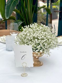 the table is set with white flowers in a vase and place card holders on it