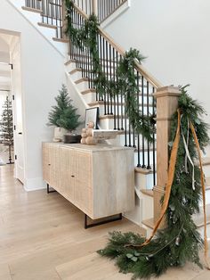 a christmas garland is tied to the banister and next to a wooden cabinet with pine cones on it