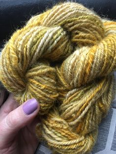 a hand holding a skein of yarn in yellow and brown colors on a gray surface