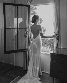 a woman in a wedding dress looking out the window