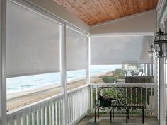 a porch with white blinds and a bench on the front porch overlooking the beach in the background