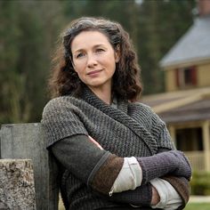 a woman with her arms crossed leaning against a wooden post