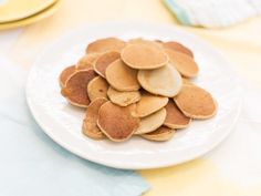 a white plate topped with lots of pancakes on top of a table next to yellow plates