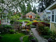 a garden with lots of trees and flowers in front of some small houses on the other side