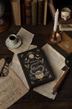 an open book sitting on top of a wooden table next to glasses and a candle