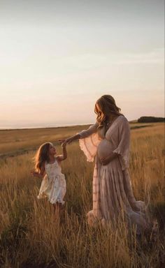 a mother and daughter holding hands while walking through tall grass in the field at sunset