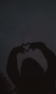 the silhouette of a woman making a heart with her hands