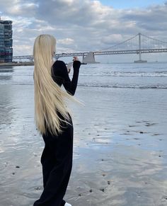 a woman with long blonde hair is standing on the beach and looking at the water