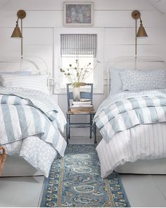 two beds in a bedroom with blue and white bedding, rugs and lamps