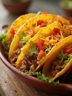 three tacos in a bowl with lettuce, tomatoes and cheese on top