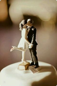 a bride and groom figurine standing on top of a cake with their arms around each other