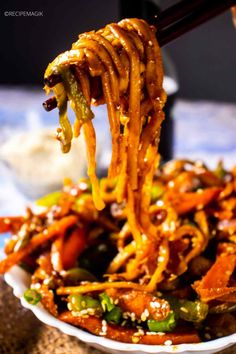 a bowl filled with noodles and vegetables being held up by chopsticks over it