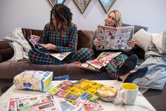 two women sitting on a couch reading newspapers