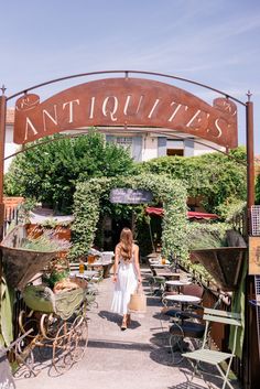 a woman is walking under an antique sign in front of some tables and lawn chairs