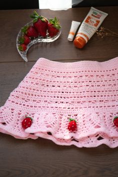 a pink crocheted blanket with strawberries on it next to some other items