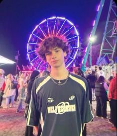 a young man standing in front of a ferris wheel at an amusement park during the night