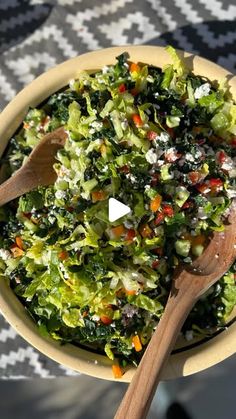 a bowl filled with salad and wooden spoons sitting on top of a checkered table cloth