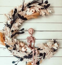 a skeleton wreath on a white wooden wall with dried leaves and pumpkins in it