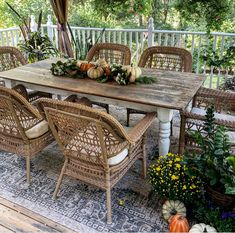 an outdoor dining table with wicker chairs and pumpkins on the top, surrounded by greenery