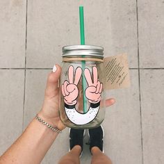 a person holding up a mason jar with two fingers painted on it and a green straw