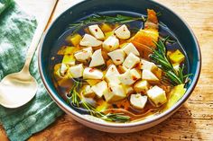 a bowl of soup with potatoes, carrots and herbs in it on a wooden table