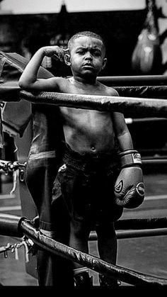 a black and white photo of a young boy with boxing gloves on his head standing in the ring