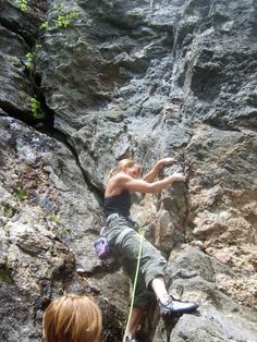 a man climbing up the side of a mountain with his hands in the air while another person holds on to him