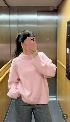 a woman taking a selfie in an elevator wearing a pink sweater and grey pants