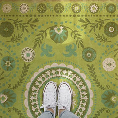 a person standing in front of a green rug with flowers and leaves on the floor