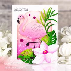 a pink flamingo card with white flowers and green leaves on it, sitting next to some white daisies