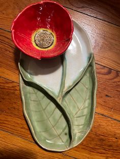 a red flower sitting on top of a green leaf shaped plate next to a wooden floor