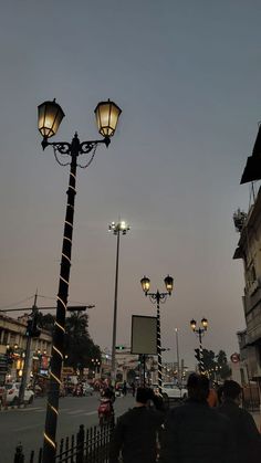 people are walking down the street in front of some lamps and buildings at night time