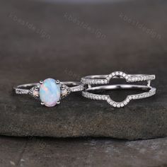 two opal and diamond rings sitting on top of a rock