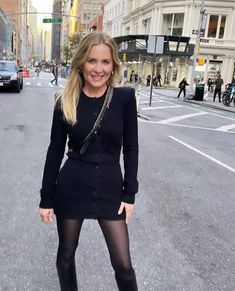 a woman standing in the middle of a street wearing black tights and knee high boots