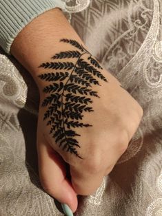 a person's hand with a black fern tattoo on their left wrist and the other hand is holding a pencil