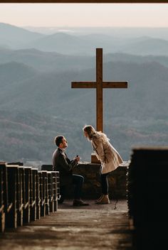 a man kneeling down next to a woman in front of a cross