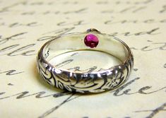 "Beautiful handmade ring. Constructed completely in sterling silver. The gemstone is a 3.5mm created ruby that has been bezel set. Perfect gift for a July birthday. The band of the ring has a lovely floral pattern on it which gives it a \"Renaissance\" look. This ring is so lovely. Can be worn by itself or as stack rings. Rings are \"made to order\". Generally it will take 2-3 days to complete unless there is a \"special request\" involved. This listing is for one ring only. The gemstone bands c Engraved Sterling Silver Ruby Ring, Unique Ruby Ring With Bezel Setting For Anniversary, Heirloom Silver Ruby Birthstone Ring, Silver Ruby Ring With Bezel Setting, Engraved Ruby Ring As Gift, Engraved Ruby Ring Gift, Bezel Set Ruby Ring, Stack Rings, July Birthday